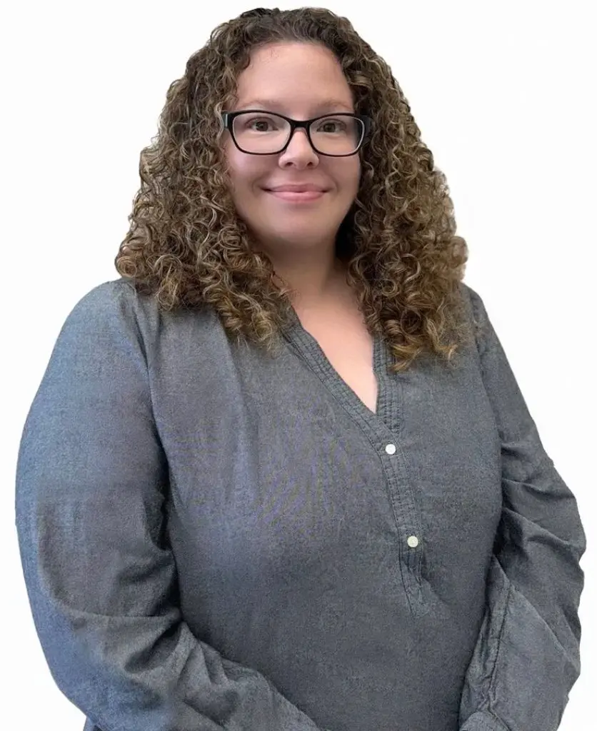 A woman with glasses and long hair wearing a gray shirt.