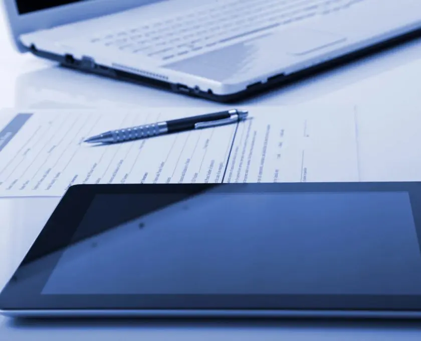 A tablet and laptop on top of papers.