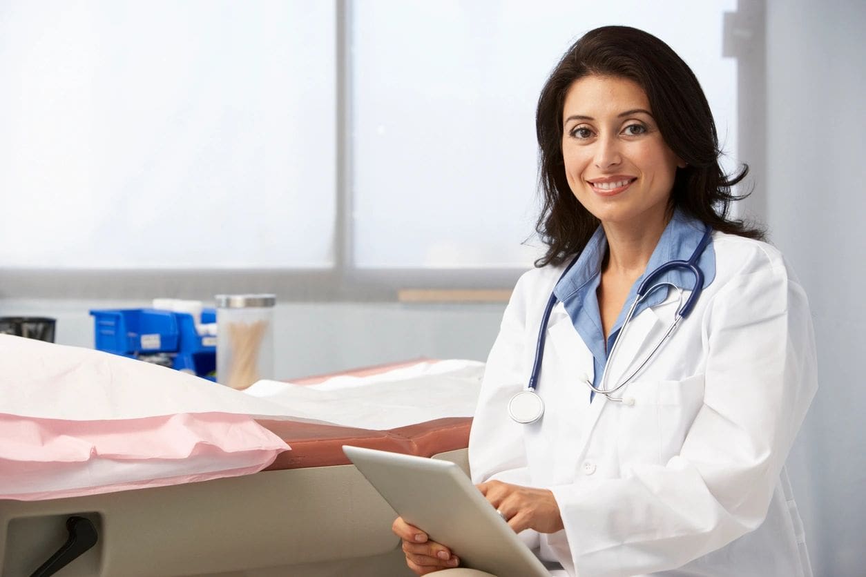 A woman in white lab coat holding a tablet.